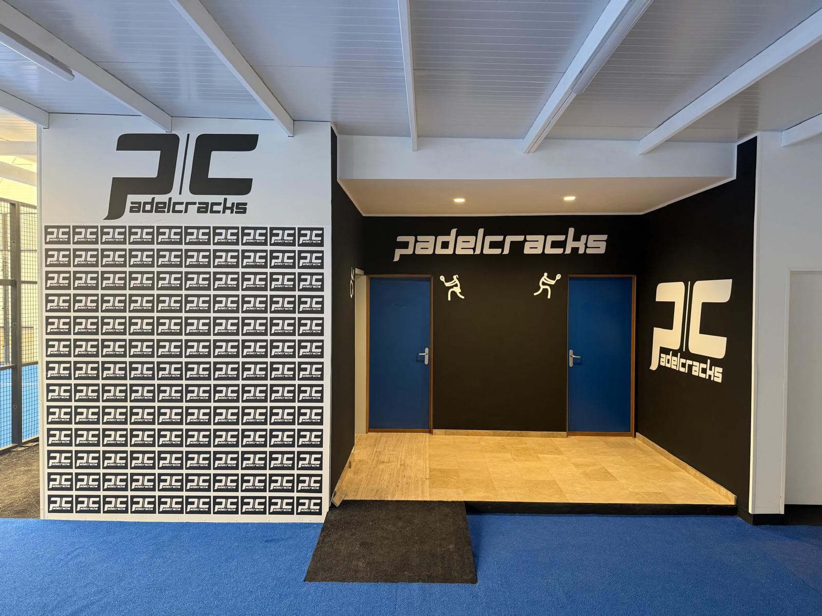La entrada a los dos vestuarios: dos puertas azules bajo el rótulo de Pádel Cracks, sobre la moqueta azul